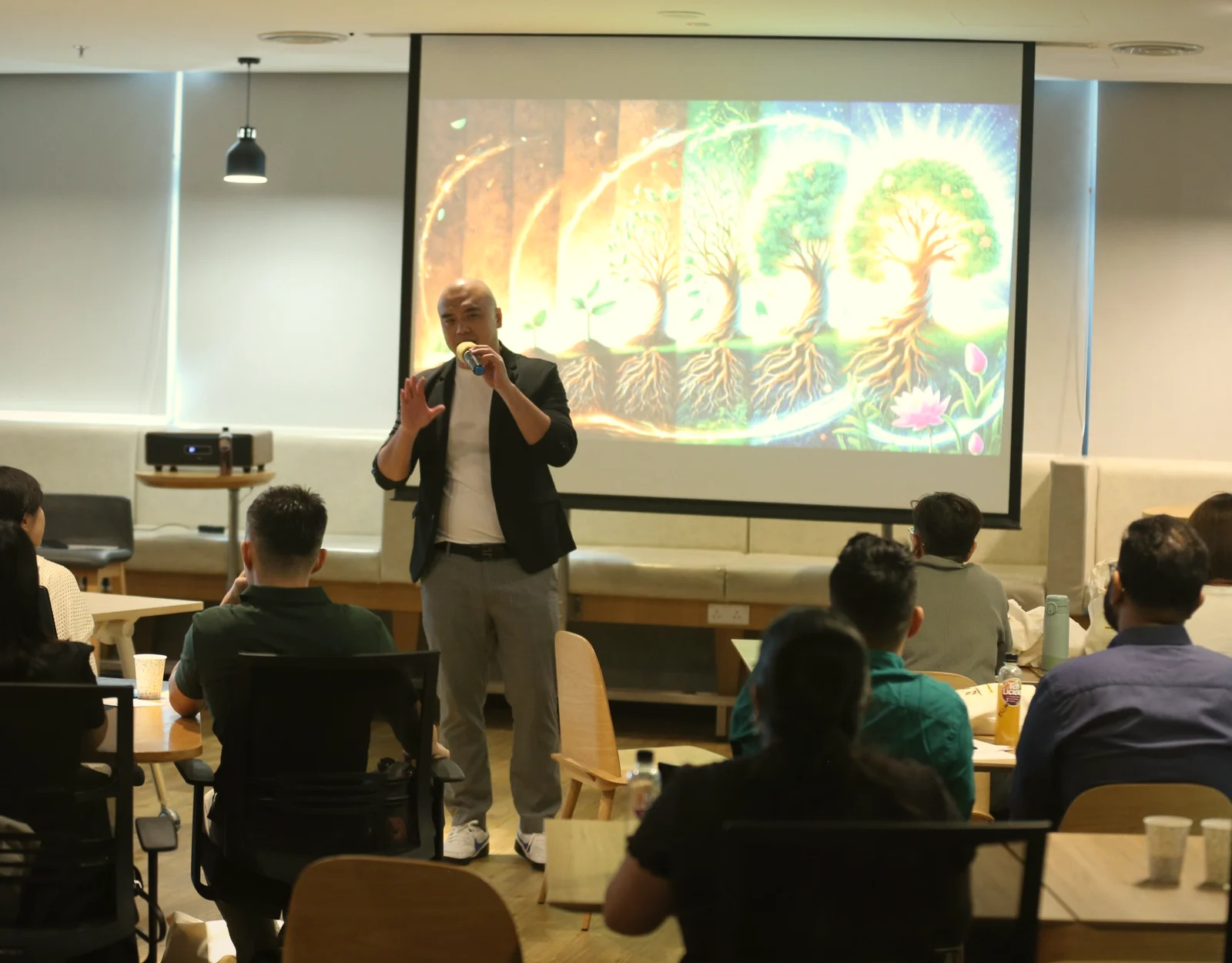 Zhi-Harn speaking to a workshop, a seed-to-tree illustration on the screen behind him